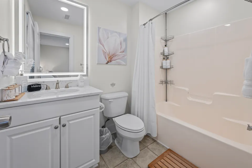 Bathroom with a backlit LED vanity mirror, marble-look counter, and a tiled tub-shower combo
