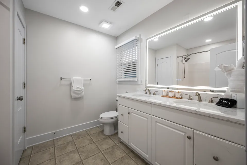 Bathroom with a backlit LED vanity mirror, white cabinetry, and neutral tile flooring