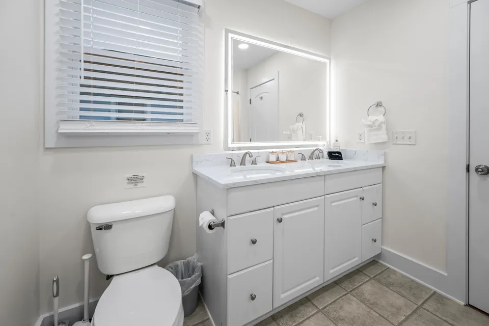 Primary ensuite bathroom with a wide backlit LED mirror, white double-door vanity, and tile flooring