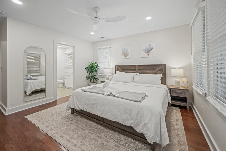King bedroom with a wood-look headboard, tan area rug, and an arched mirrored doorway opening to the ensuite bathroom