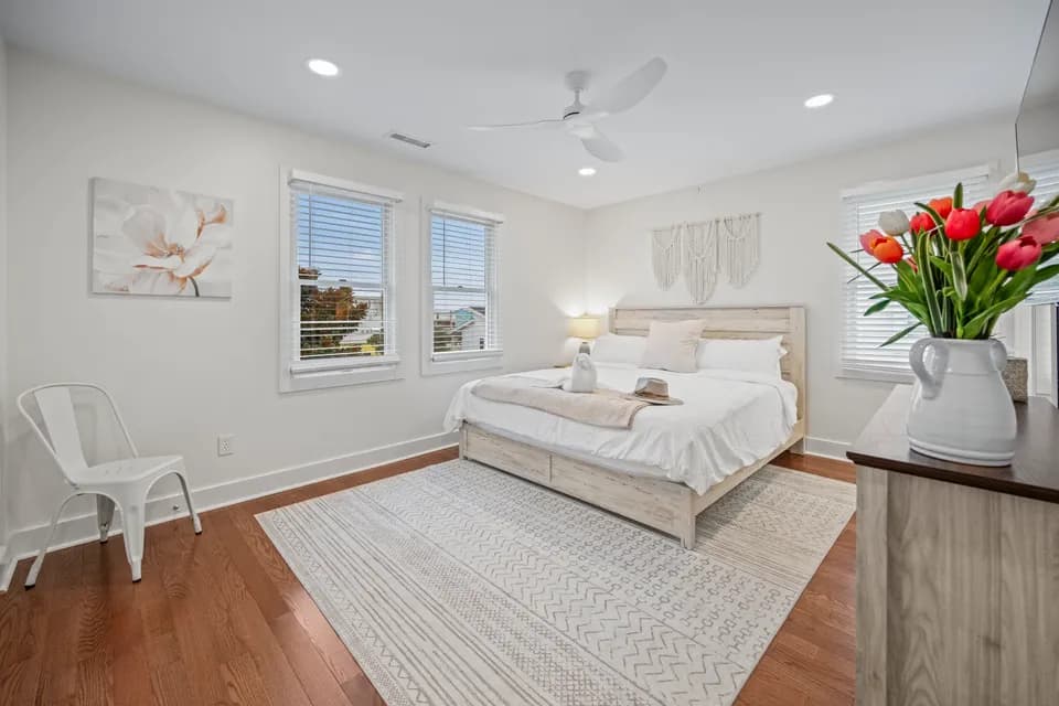 Bedroom with a light wood bed frame, white bedding, botanical magnolia art, and a woven wall hanging above the headboard