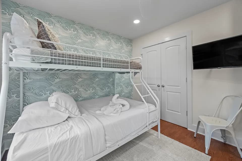 Themed bunk room with a white twin-over-full bunk bed against blue wave-pattern wallpaper, a wall-mounted TV, and white closet doors