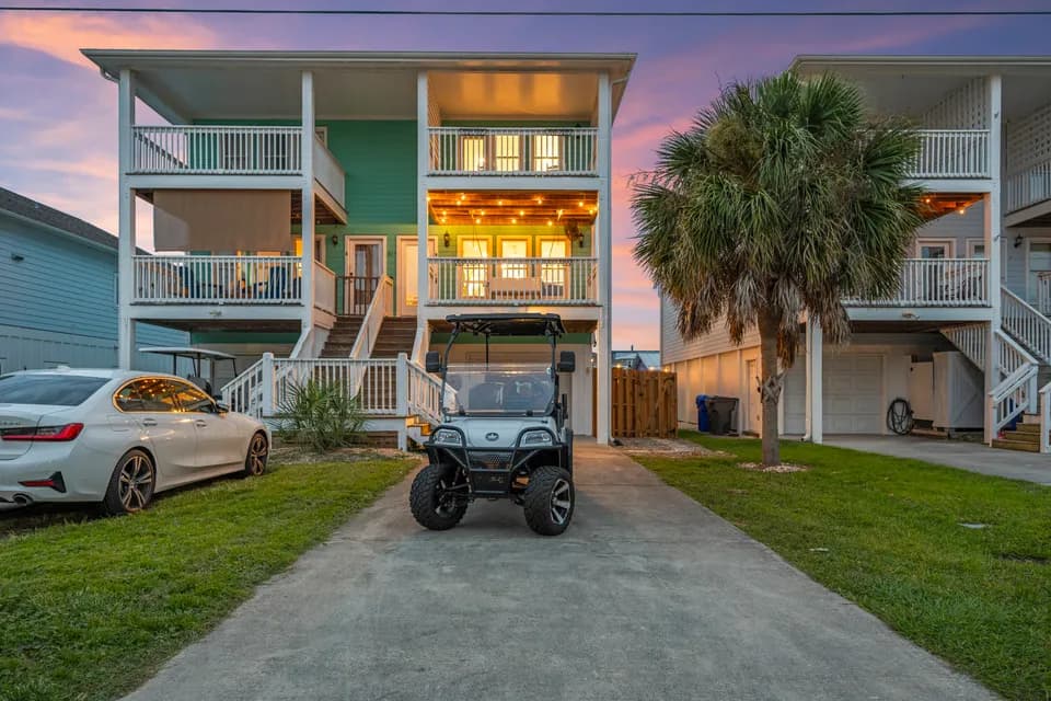Front of Magnolia by the Sea at dusk with a car and golf cart parked beneath a palm tree near the covered entry