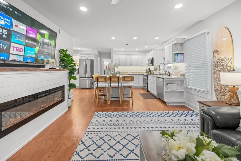 Open-concept great room looking from the fireplace and TV through to the white-cabinet kitchen beyond