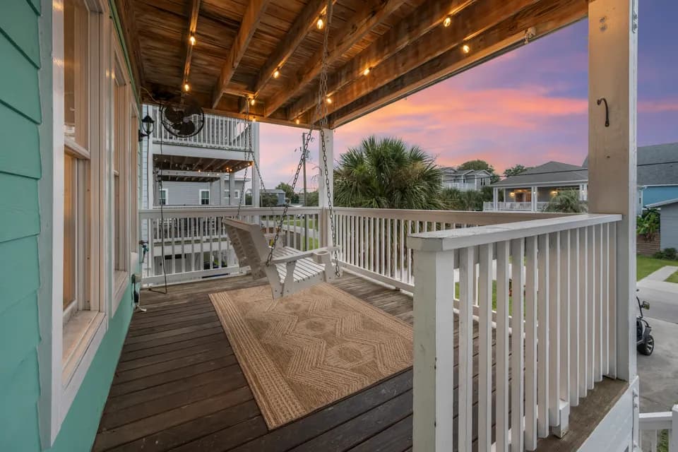 Covered ground-floor porch at twilight with a rocking chair and string lights strung overhead