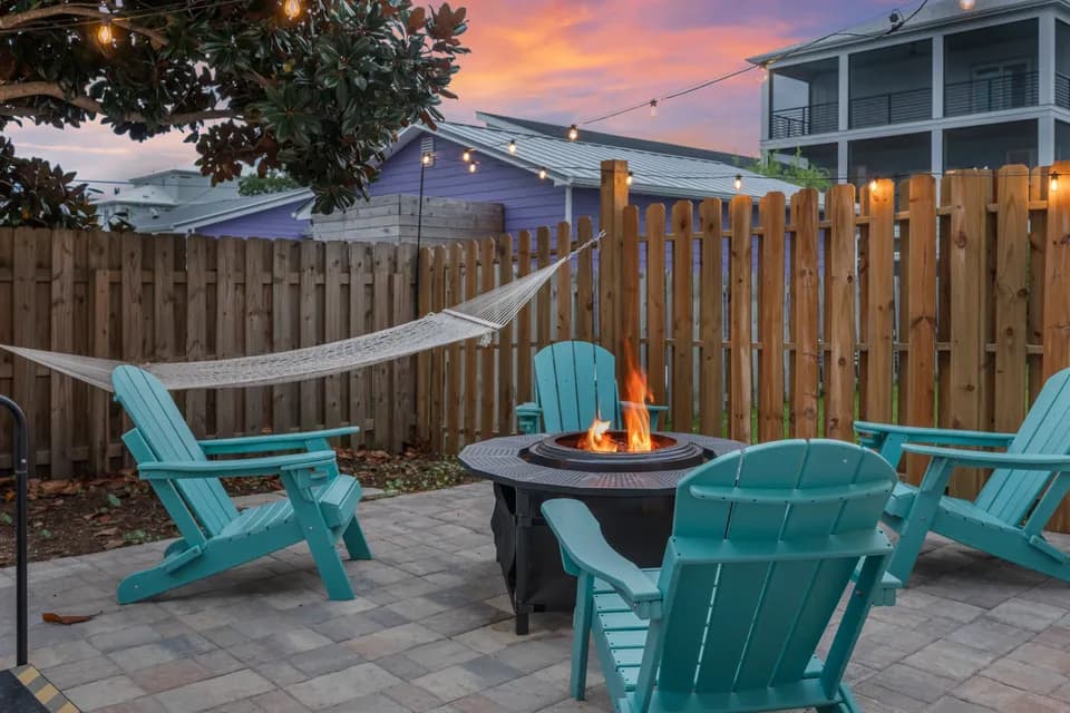 Close view of the fire pit burning at dusk, ringed by teal Adirondack chairs on the paver patio